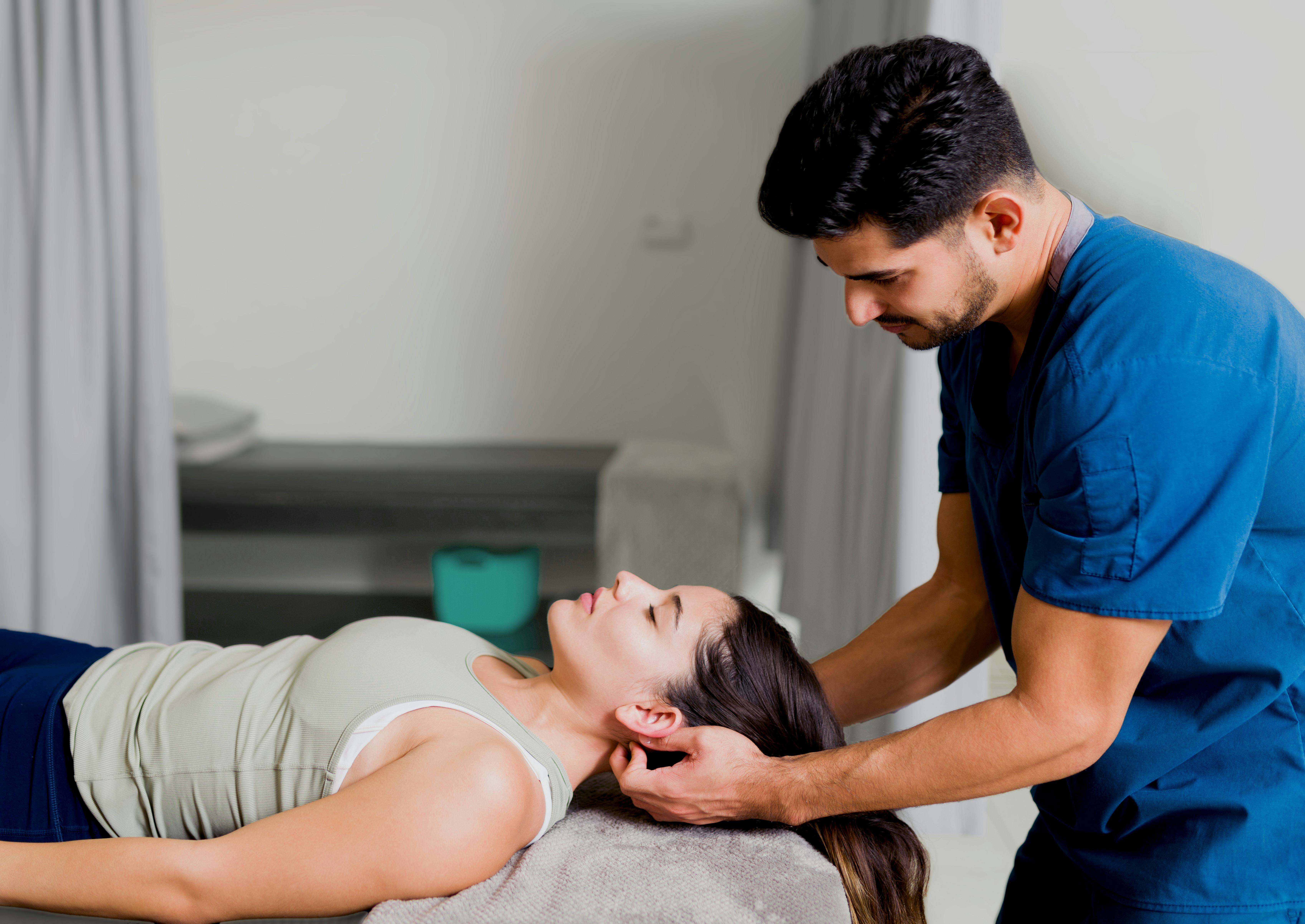A woman is lying on her back on a massage table, receiving a neck massage from a masseur.