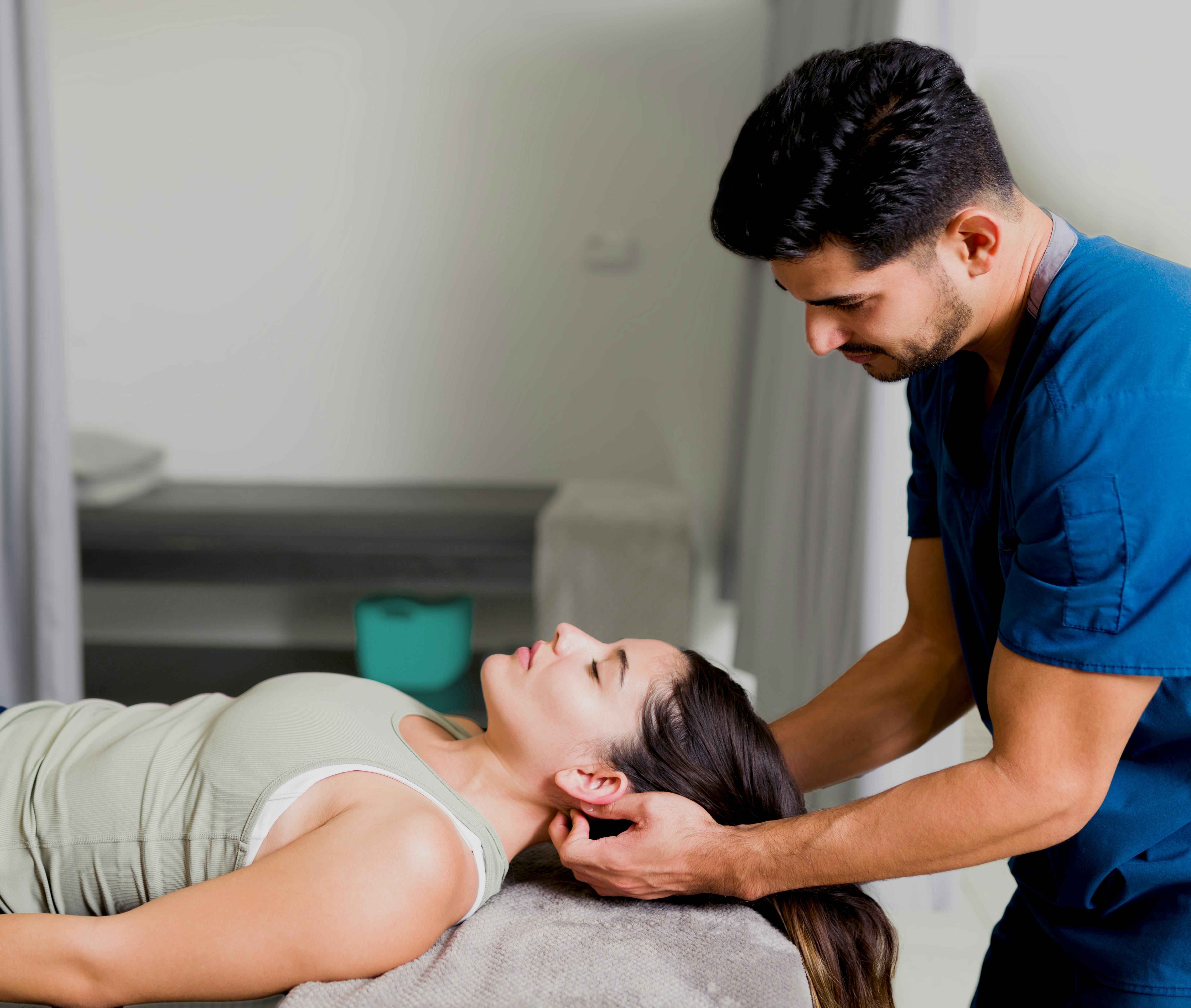 A woman is lying on her back on a massage table, receiving a neck massage from a masseur.