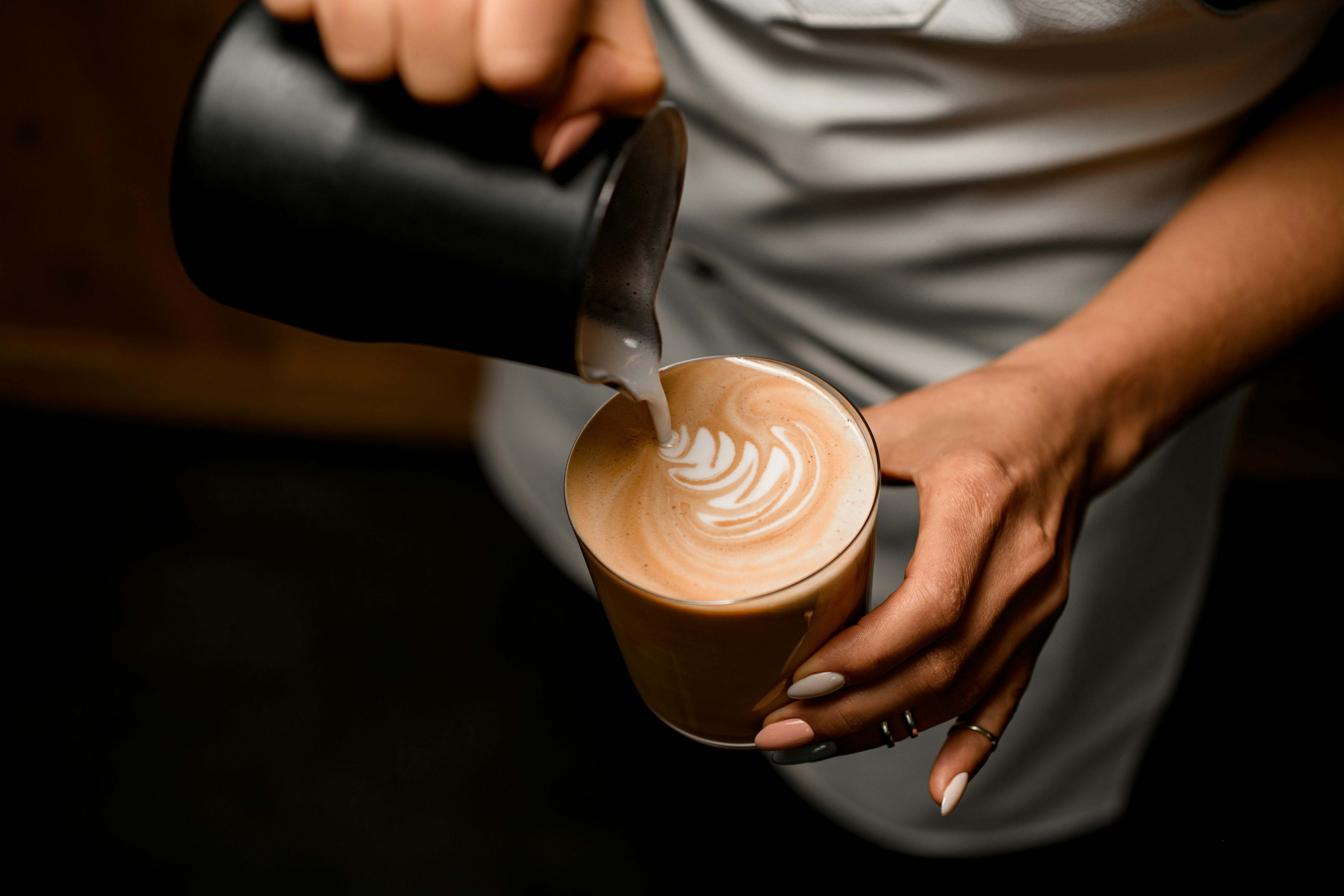 A person is pouring cream onto a cup of coffee, making coffee art.