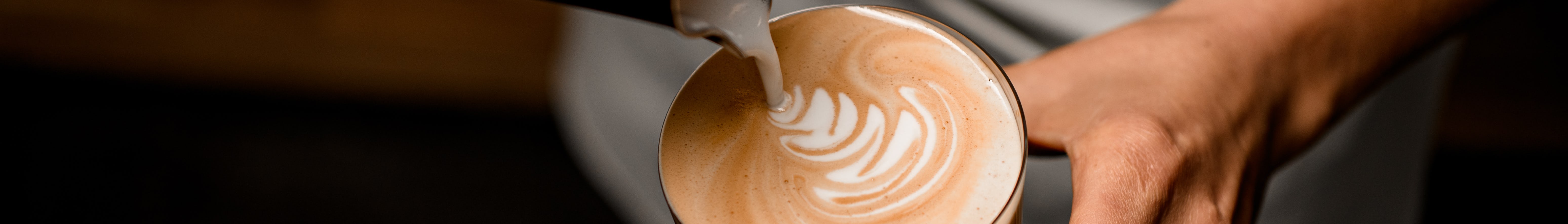 A person is pouring cream onto a cup of coffee, making coffee art.