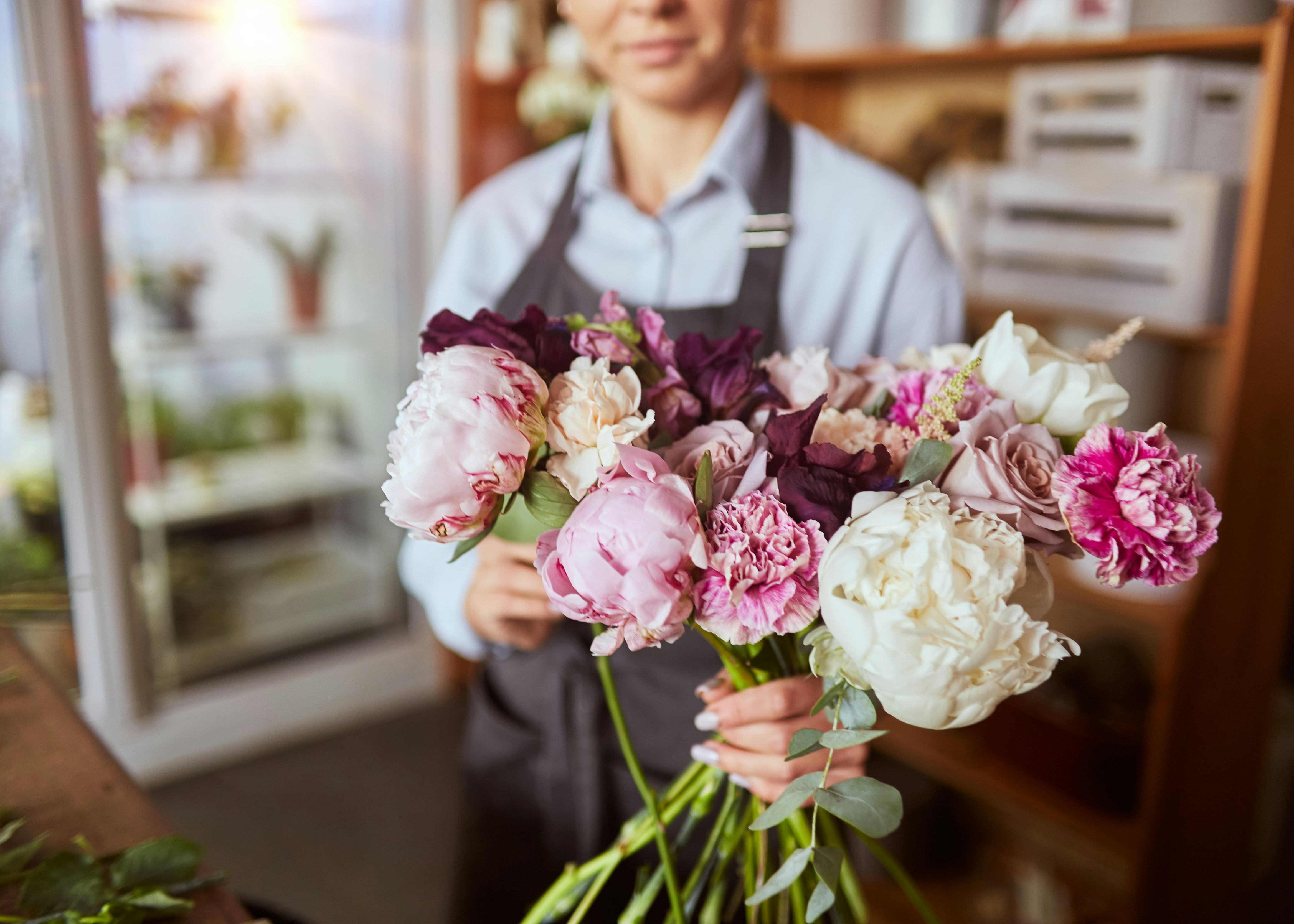 An employee in an apron is holding out a bunch of pink and white flowers, including roses.