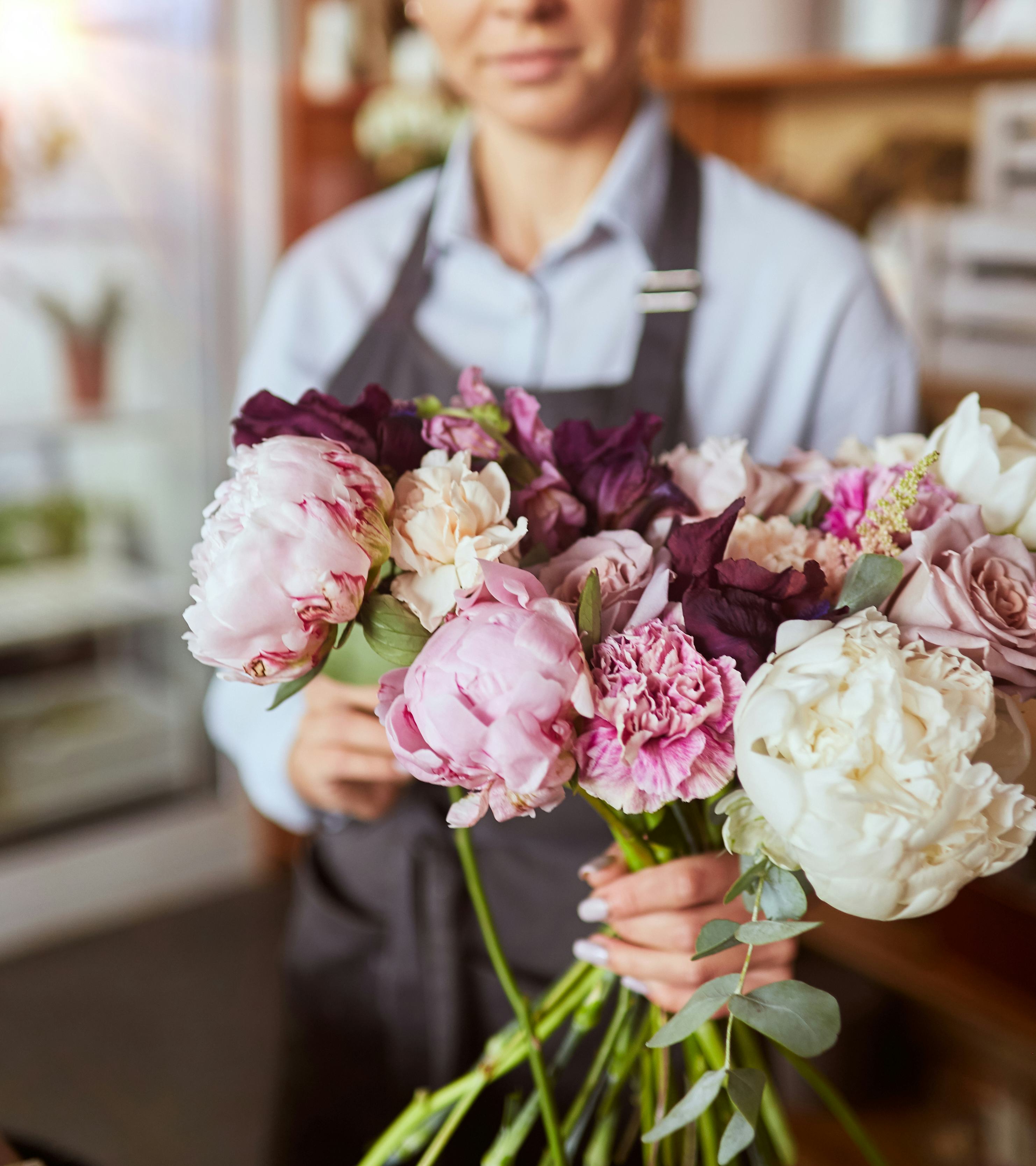 An employee in an apron is holding out a bunch of pink and white flowers, including roses.