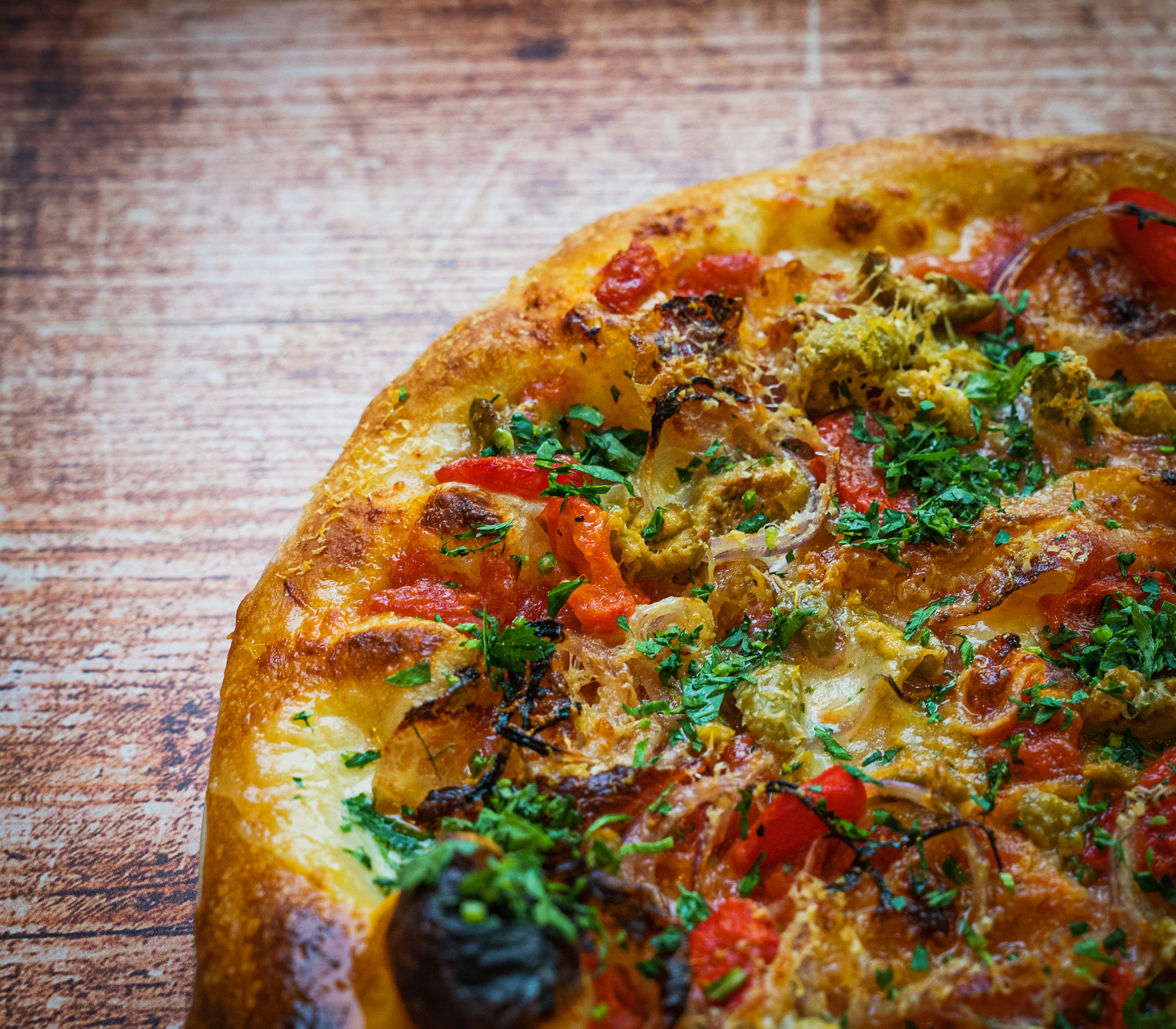 A cooked pizza with tomato, black olives, and parsley garnish.