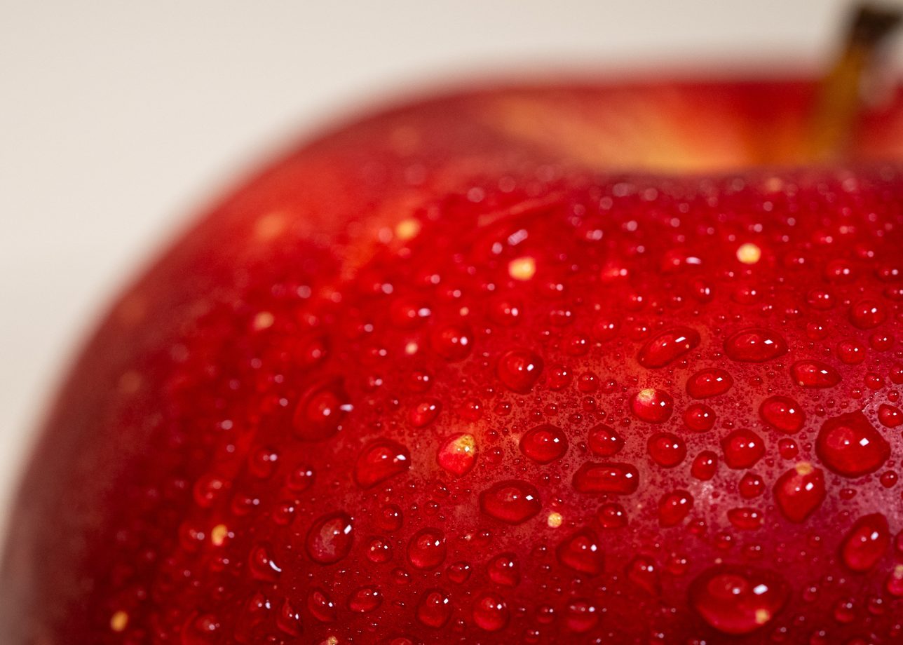 A close-up macro photo of a red apple, covered with small droplets of water.
