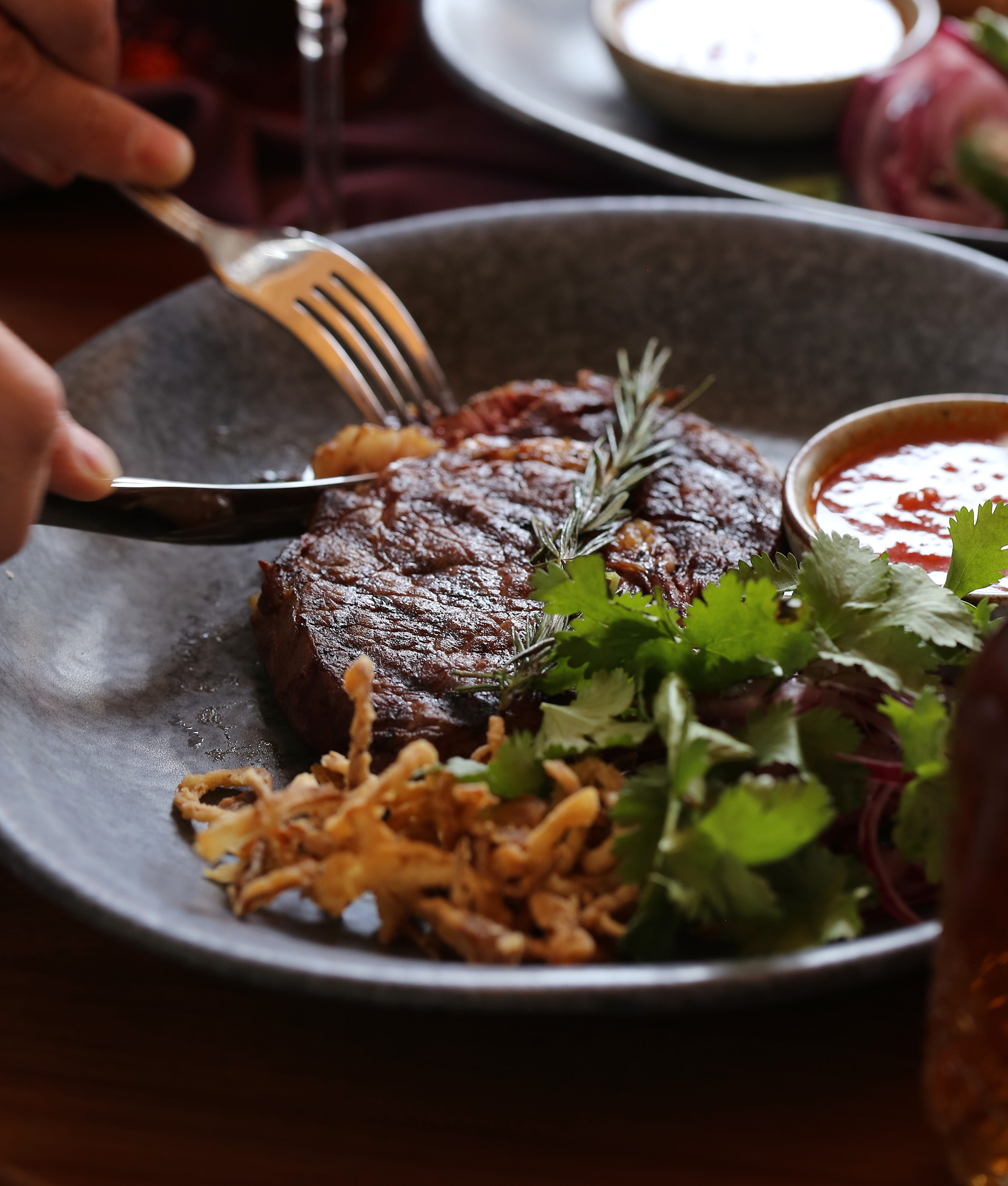 A patron cutting through a juicy steak, just their hands visible, drinking wine and about to eat a meal.